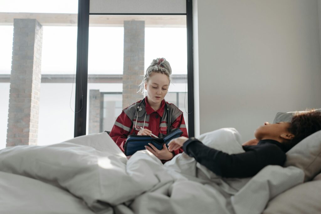 A healthcare worker takes notes while attending to a patient in bed, providing home healthcare.