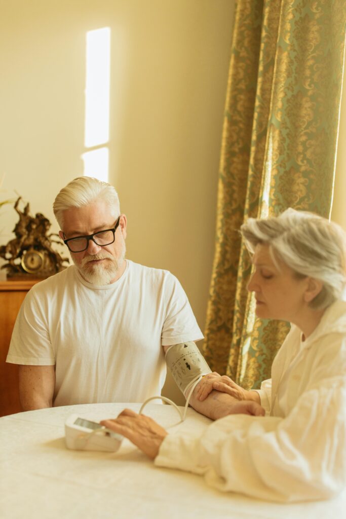 A gray-haired couple using a digital blood pressure monitor in a warmly lit room.