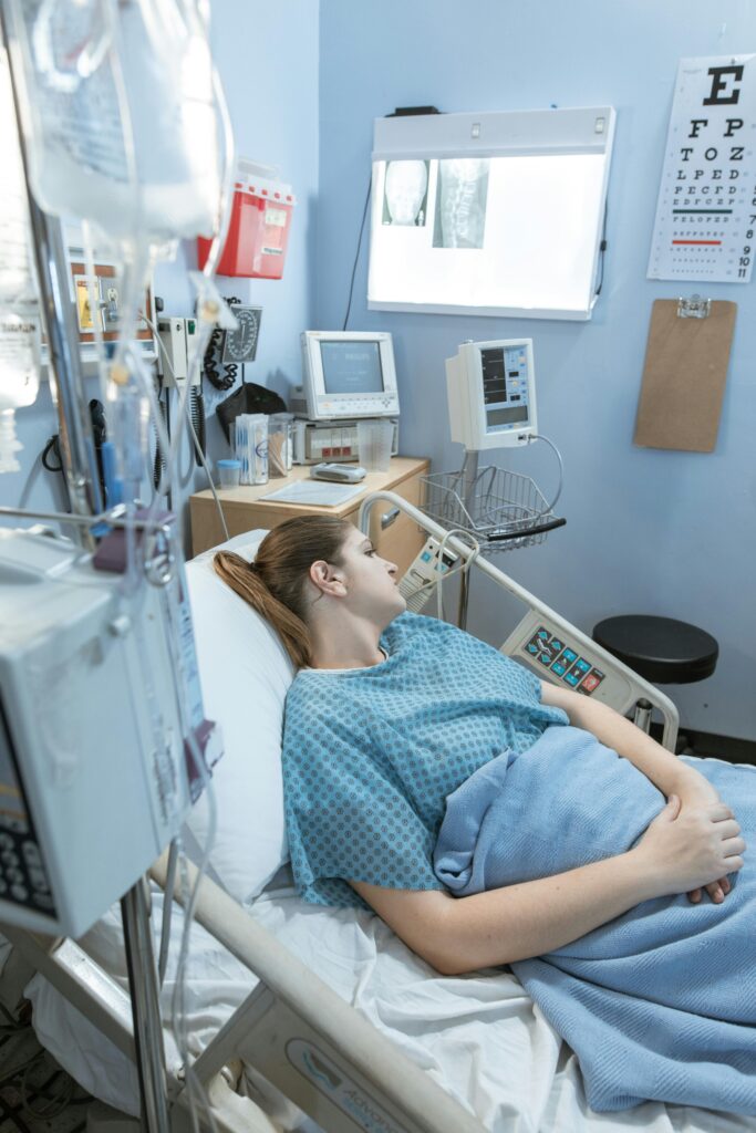 A woman lying in a hospital bed with equipment and X-rays in the background.