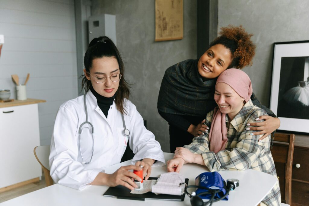 A doctor consults a cancer patient and her supportive friend in a warmly lit clinic room.