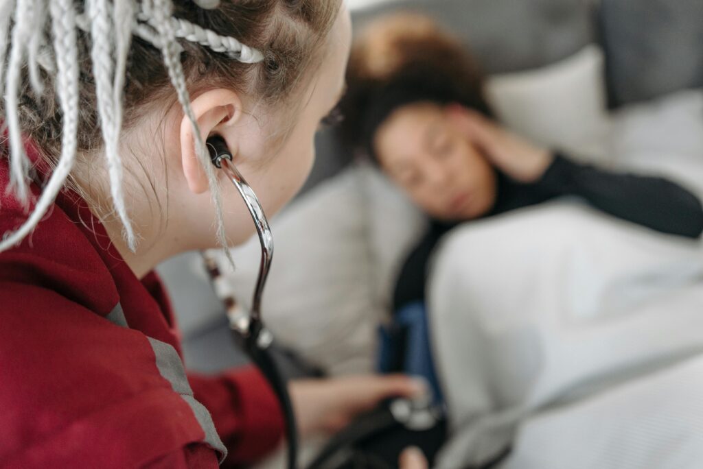 Female paramedic checking the vital signs of a patient using a stethoscope in a home setting.