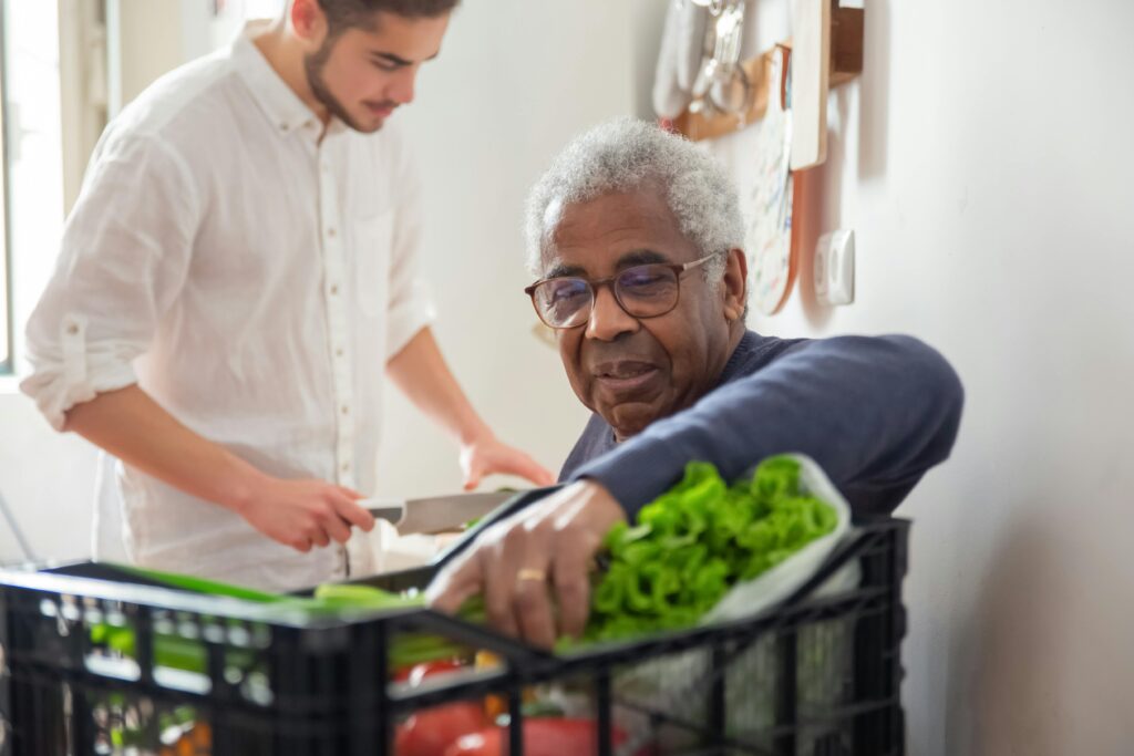 A senior man supported by a volunteer with groceries at home.