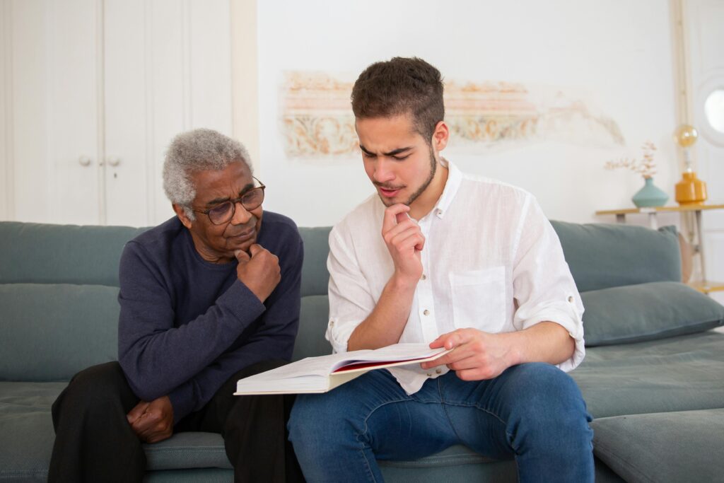 Young man and senior discussing a book at home, fostering intergenerational connection.