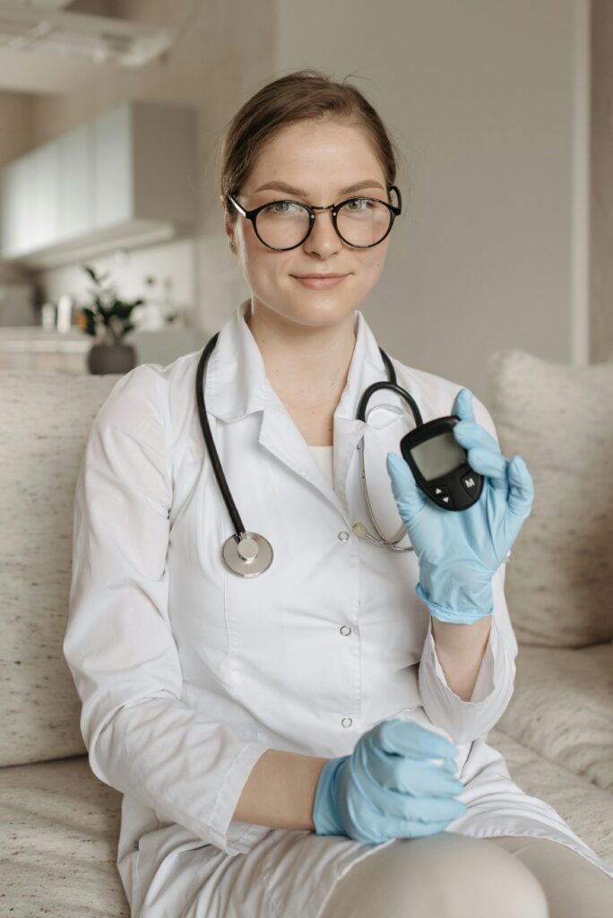 A female doctor with eyeglasses and gloves showcasing a glucometer indoors.