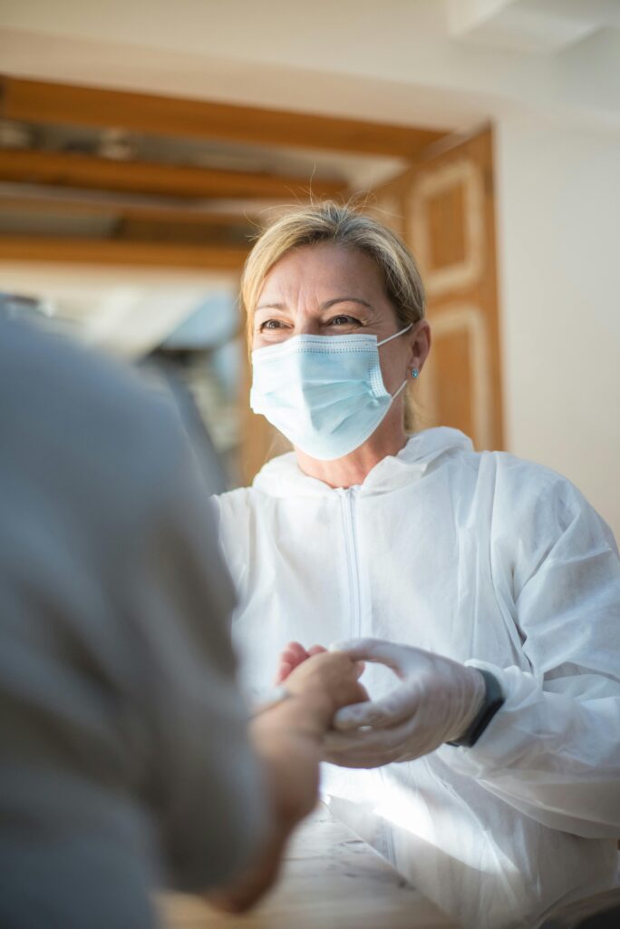 A healthcare worker in full protective gear providing care to a patient indoors.