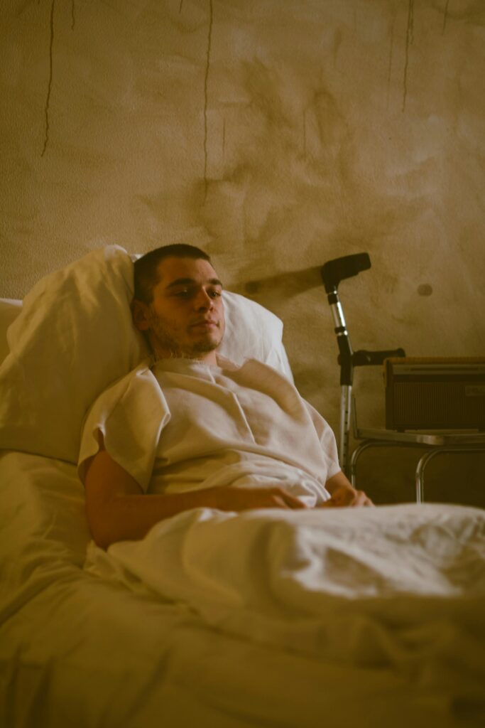 Patient lying in a hospital bed with a supportive cane beside, dim ambiance.
