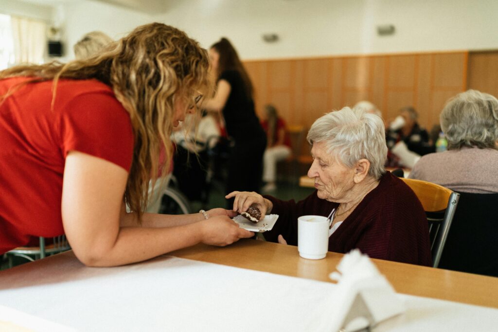 An elderly woman being assisted by a caregiver in a nursing home setting.