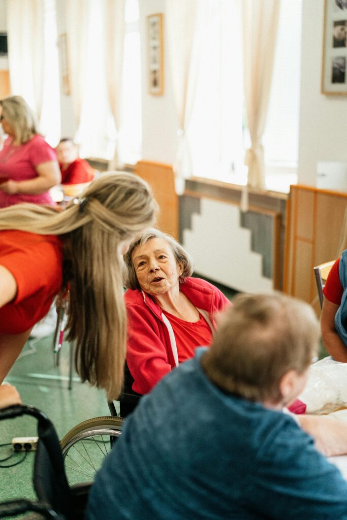 Elderly woman in a wheelchair engaging with caregiver in a bright, welcoming environment.